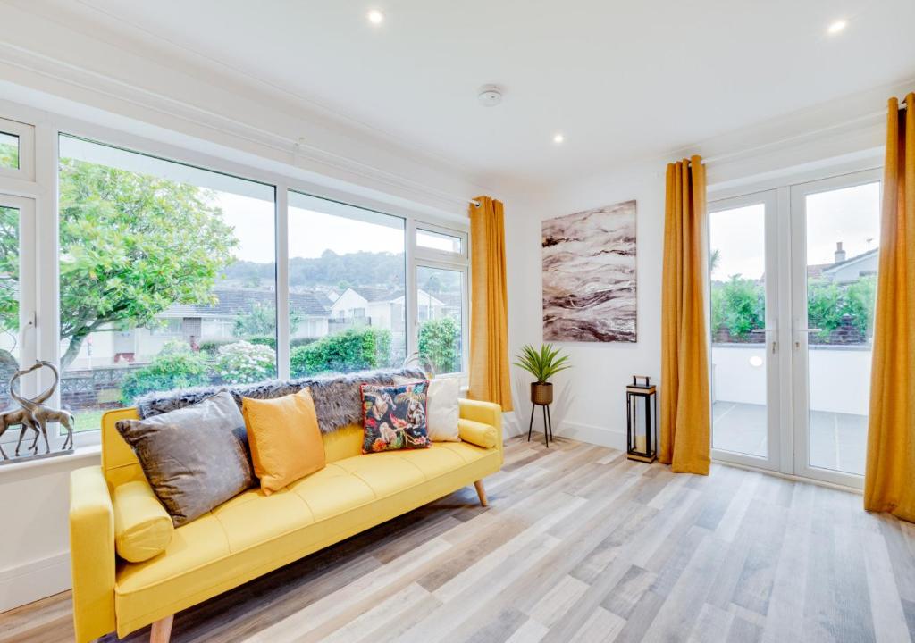 a living room with a yellow couch and large windows at Compass Rose in Brixham