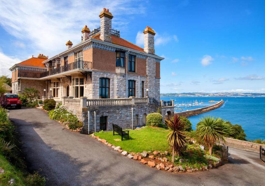 a large brick house on a hill next to the ocean at Wolborough House in Brixham