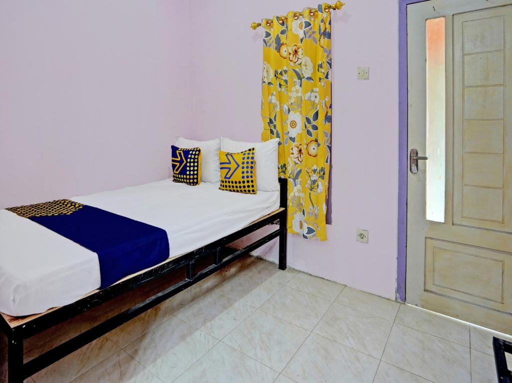małe łóżko z niebieskimi i żółtymi poduszkami w pokoju w obiekcie SPOT ON 92564 Kemangi Asri Kost w mieście Banyuwangi