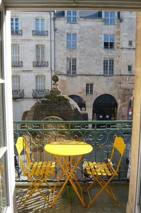une table et des chaises jaunes sur un balcon avec un bâtiment dans l'établissement Très lumineux, au coeur de la vieille ville, 86 m², à La Rochelle
