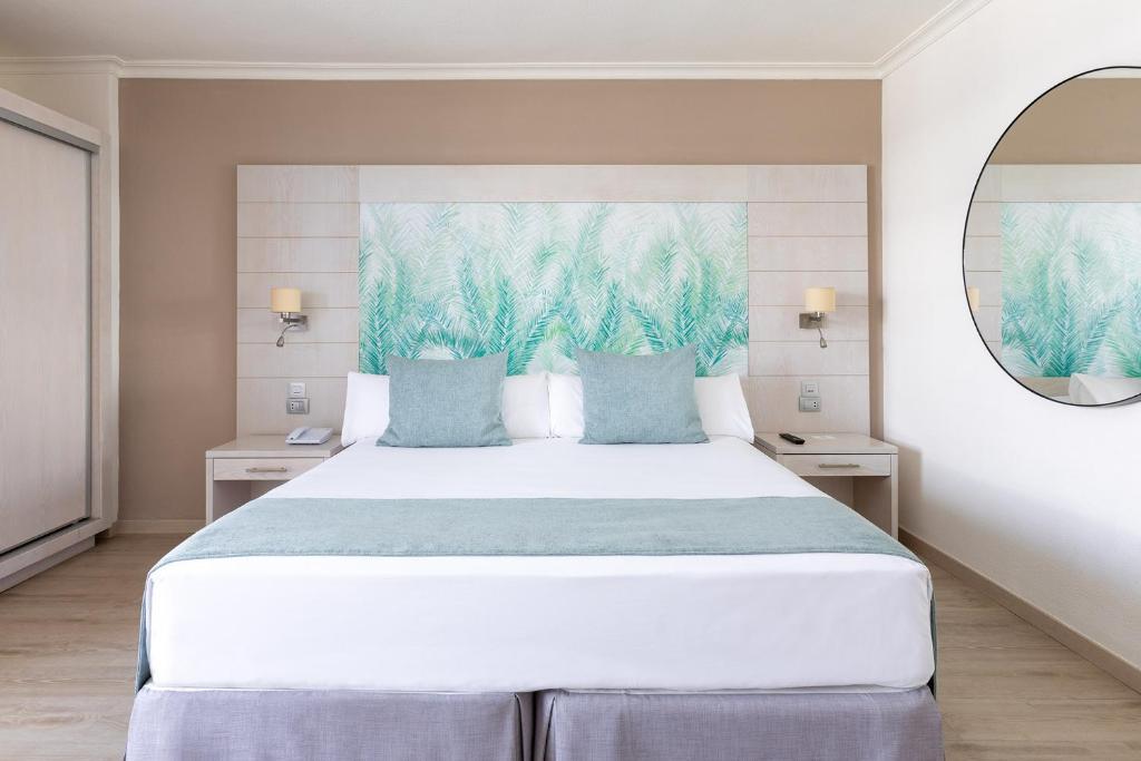 a bedroom with a large white bed with blue pillows at Tigotan Lovers & Friends Playa de las Americas - Adults Only (+18) in Playa de las Americas