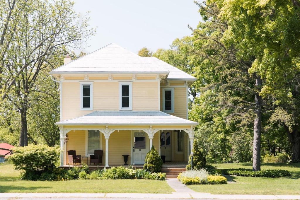 een oud geel huis met een veranda bij Watson House - Century Home near Sandbanks in Cherry Valley