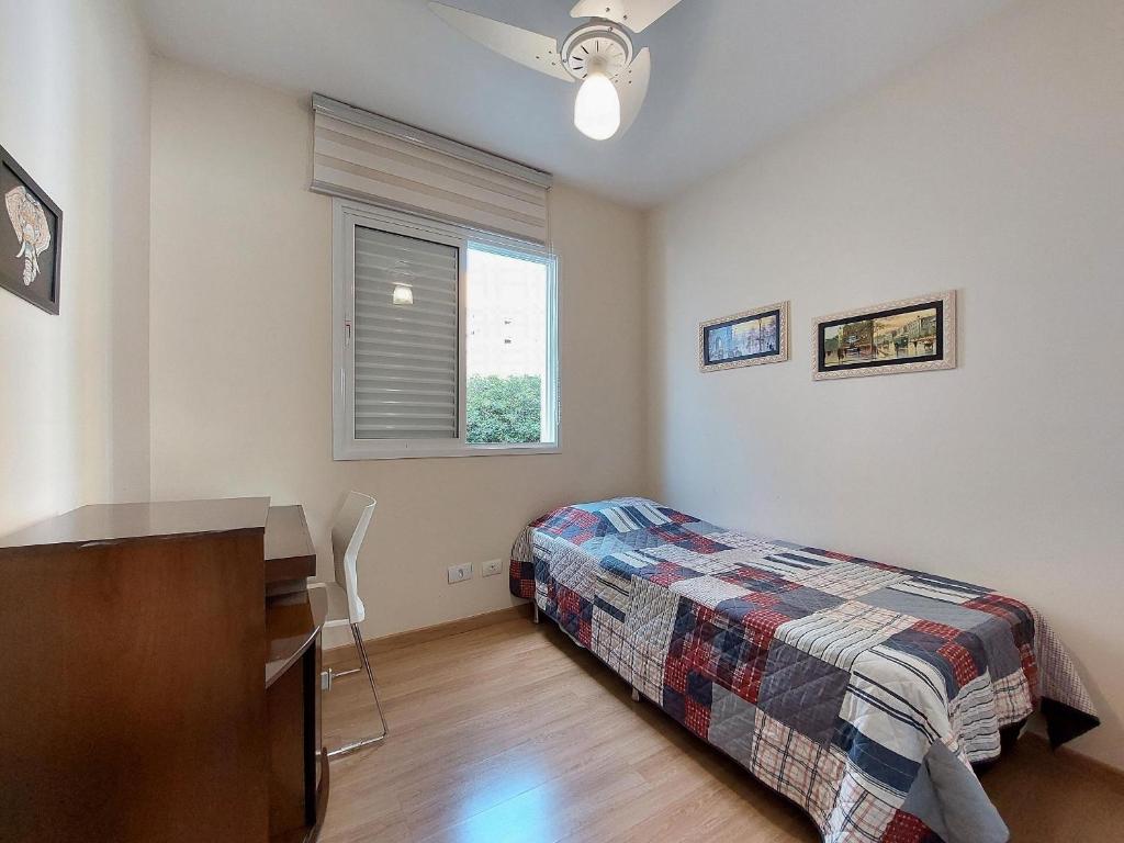 a bedroom with a bed and a desk and a window at Apto 3 quartos, sacada, churrasqueira e garagem in Londrina