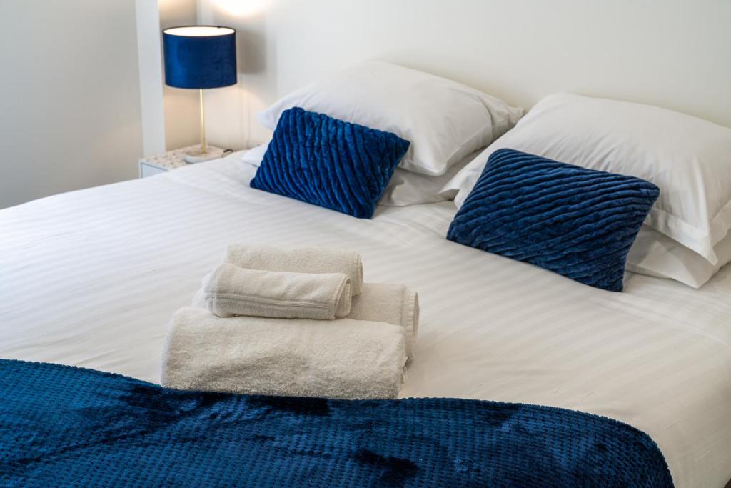 a white bed with blue pillows and towels on it at Luxury One Bedroom Serviced Apartment in the Heart of Bedford in Bedford