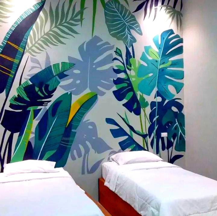 two beds in a room with a mural of leaves at Tantra Hotel in Krui