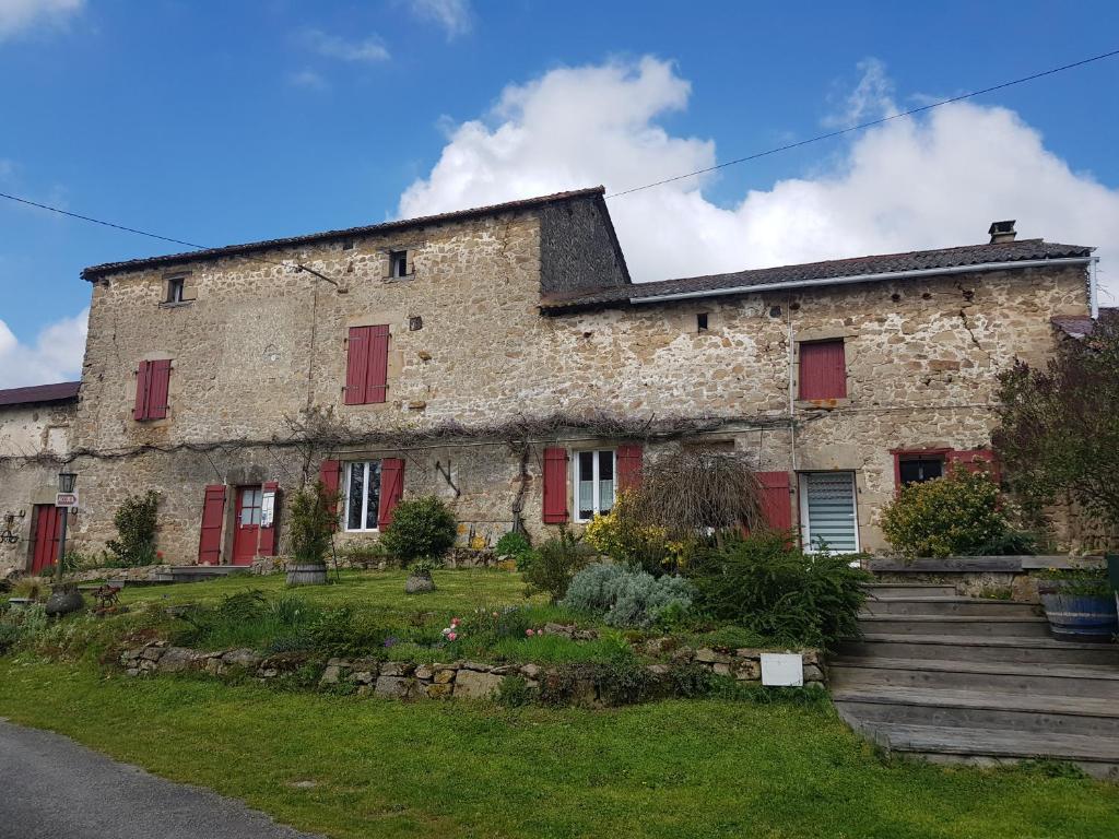 Saint-Sornin-Leulac的住宿－Les forges de Planechaud，一座古老的石头建筑,在院子里有红色百叶窗
