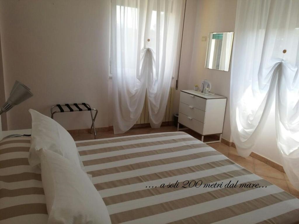 a bedroom with white curtains and a bed and a dresser at Casa Versilia Hotel in Marina di Massa