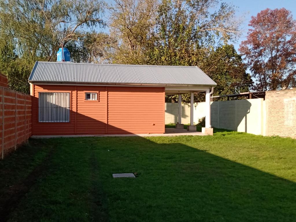 ein kleiner orangefarbener Schuppen in einem Hof mit einer Wiese in der Unterkunft El refugio in San Antonio de Areco