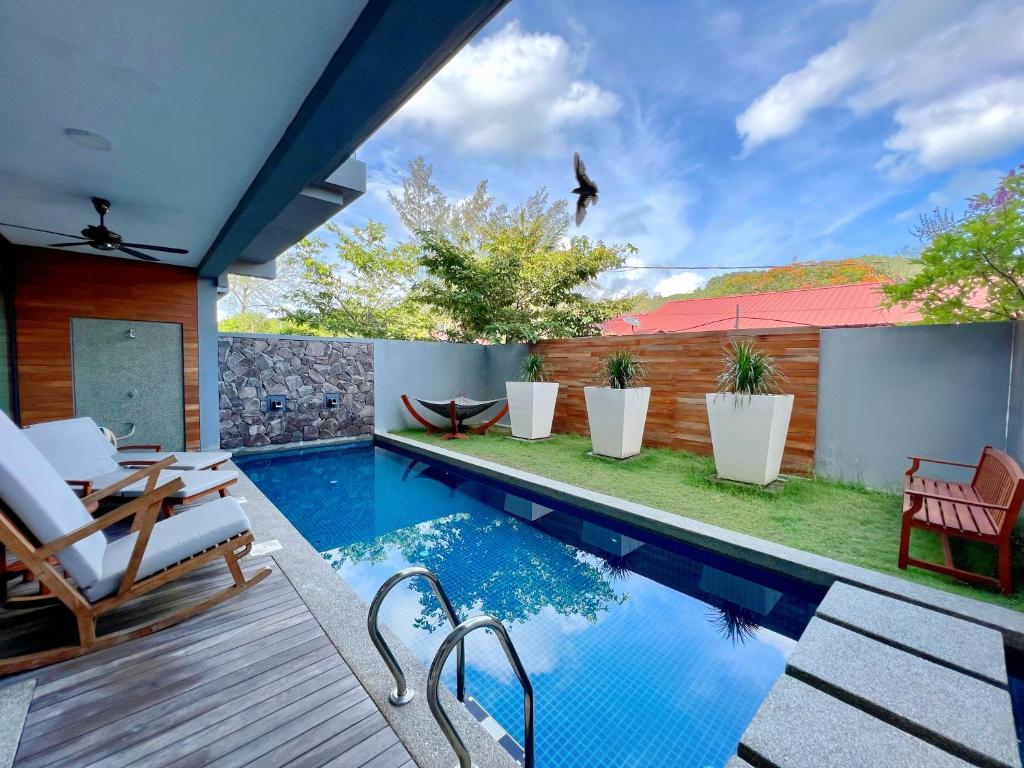 una piscina con terraza y sillas junto a una casa en Merissa Luxury Private Pool Villa en Pantai Cenang