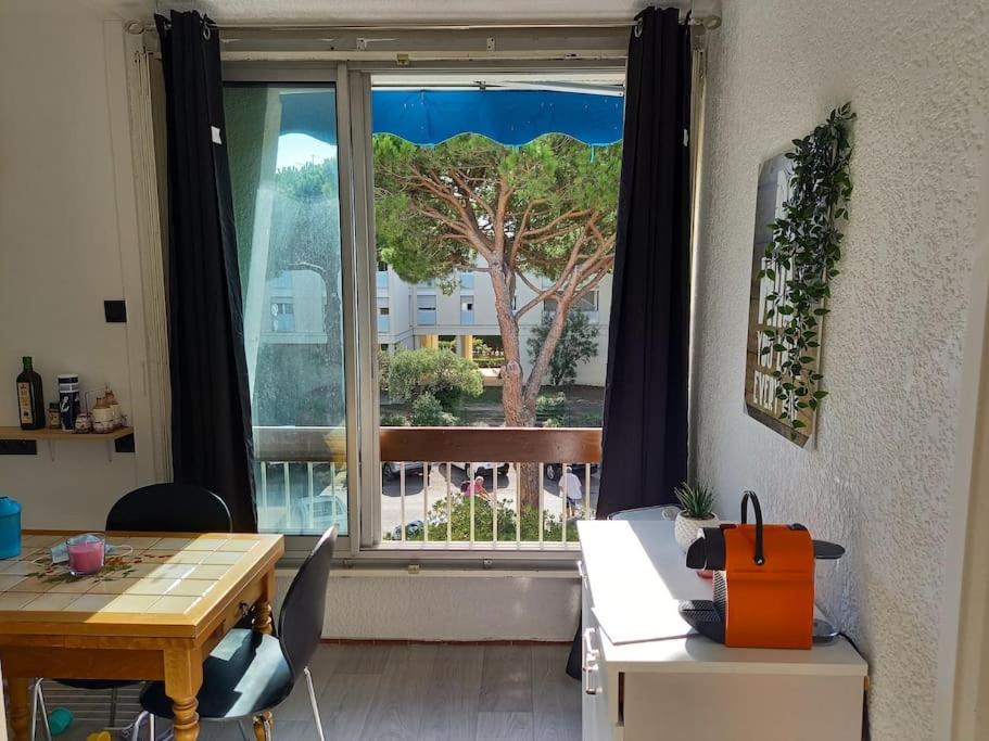 Zimmer mit einem Tisch und einem Fenster mit einem Baum in der Unterkunft studio parking privé climatisation plage proche in La Grande-Motte