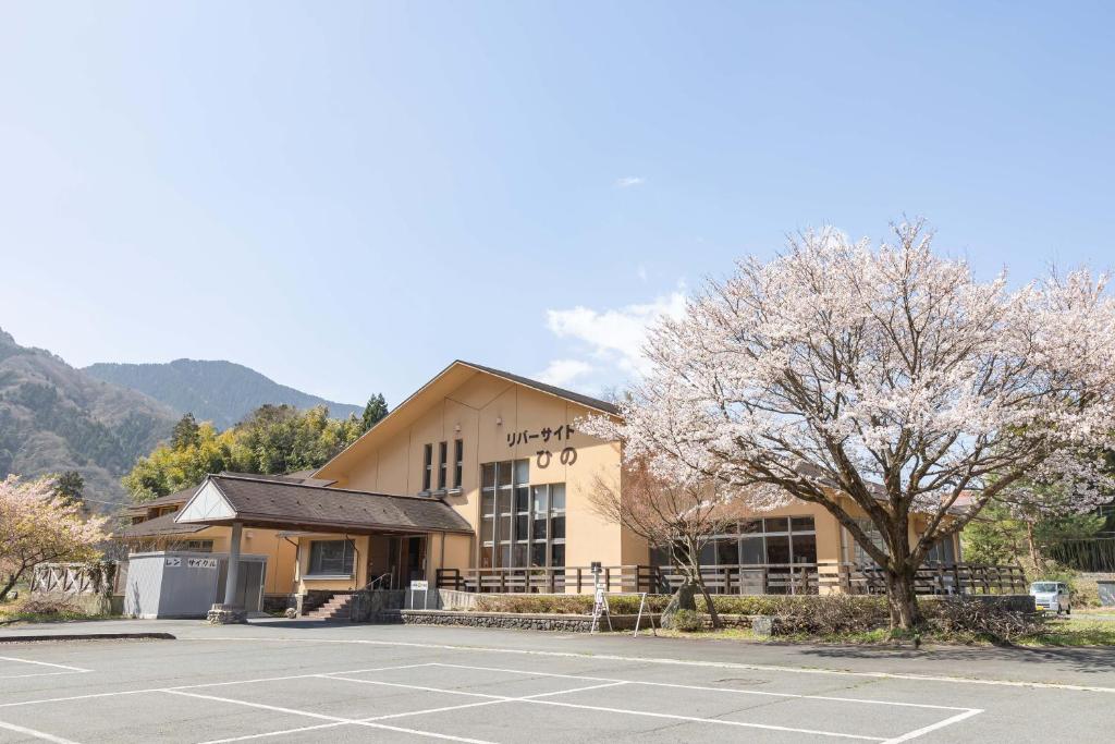 un edificio con un árbol y un aparcamiento en リバーサイドひの en Hino
