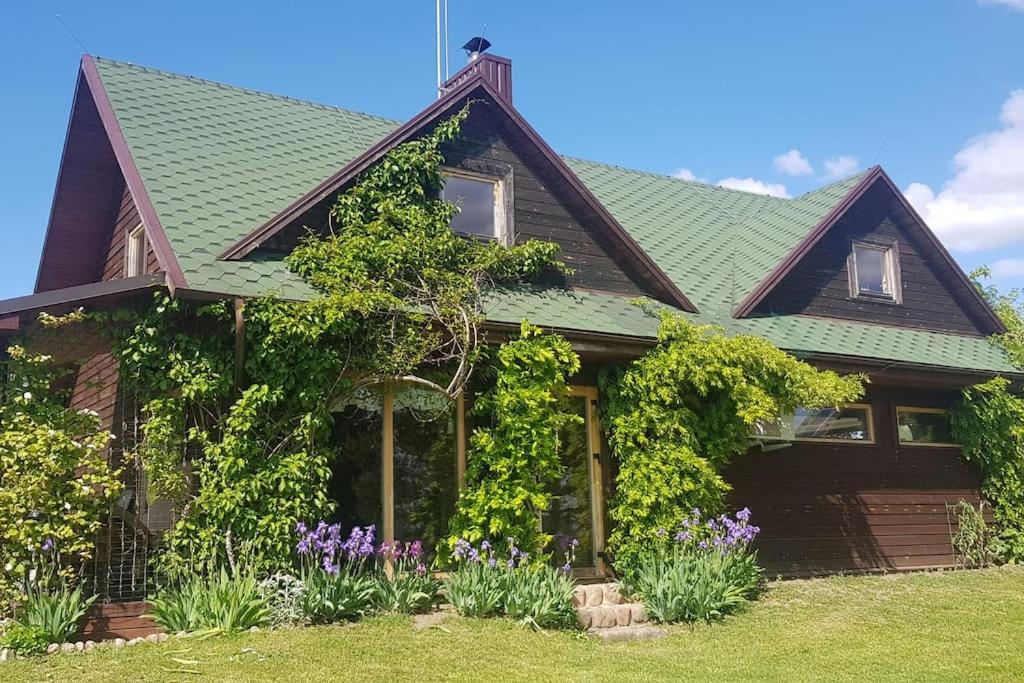 Lake Dreamhouse في Žuklijai: منزل به سقف أخضر و ورد أرجواني