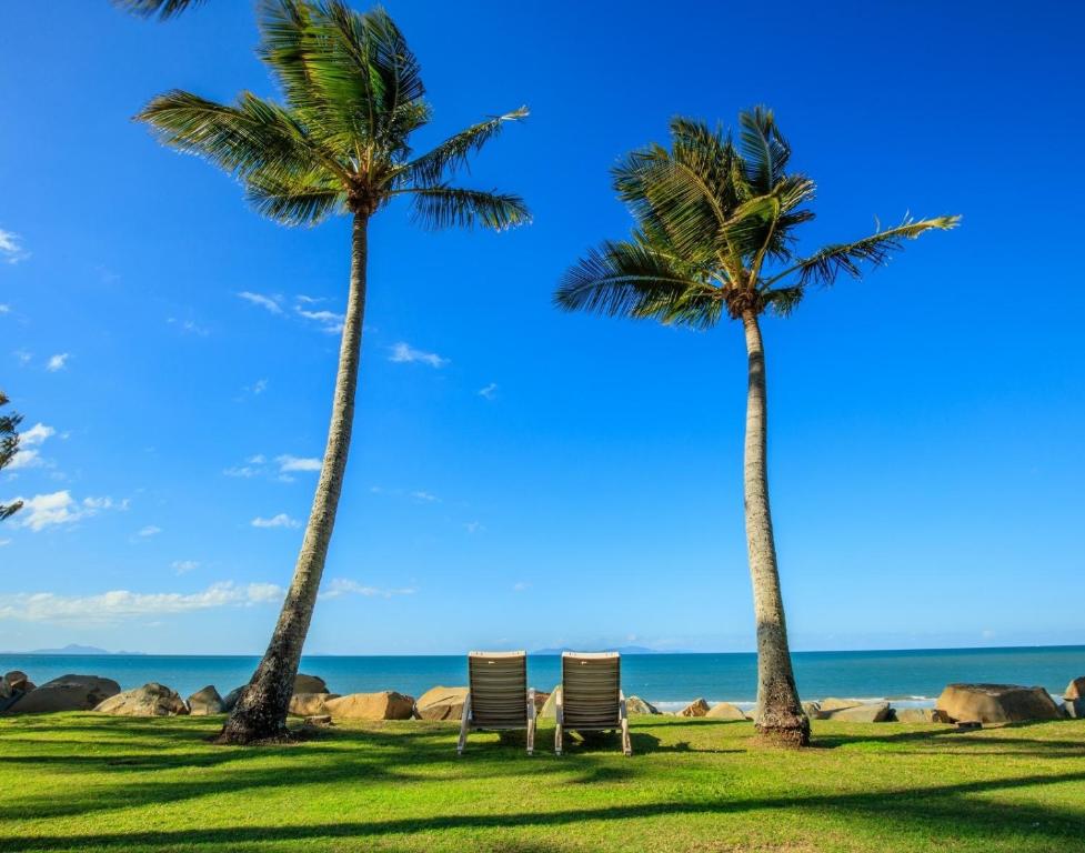 two palm trees and two chairs on the beach at ABSOLUTE BEACH FRONT MACKAY - Blue Pacific in Mackay