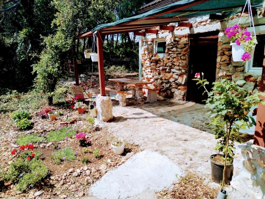 卡利的住宿－Isolated, 30m to sea, Viktoria s cottage，一座花园,花园内有一座石头房子,里面设有长凳和鲜花