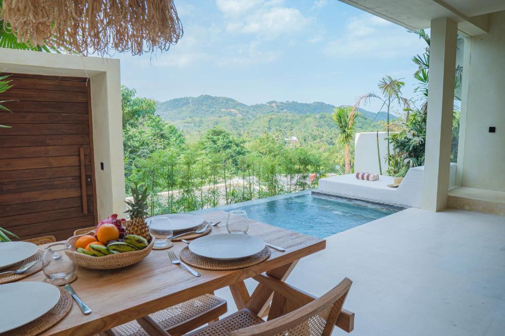 una mesa de comedor con un bol de fruta y una piscina en Olea Villas Resort en Kuta Lombok
