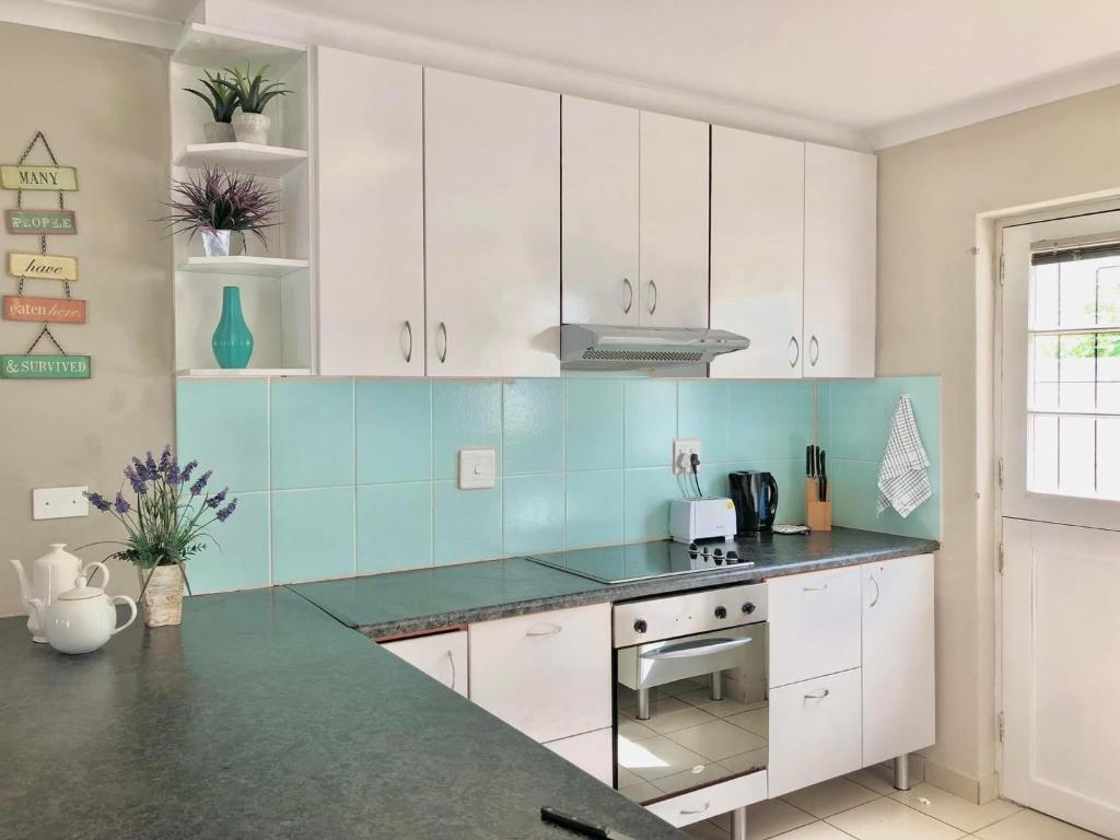 una cocina con armarios blancos y azulejos azules en Bay Breeze Guesthouse Selfcatering, en Gordonʼs Bay