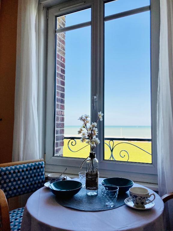 une table avec deux assiettes et un vase de fleurs sur une fenêtre dans l'établissement Les Pieds dans l'eau appartement vue mer, à Dieppe