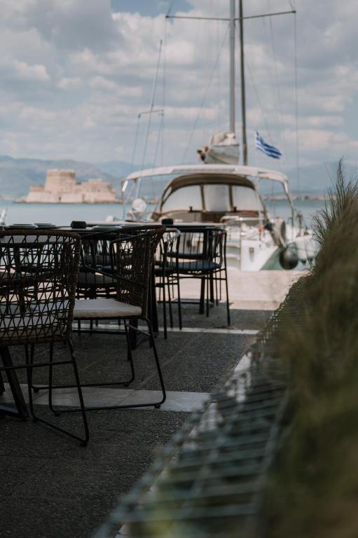 a group of chairs and tables with a boat in the water at Agamemnon Hotel in Nafplio