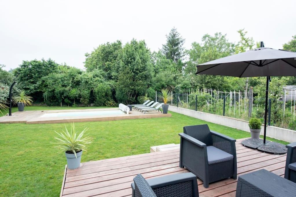 a wooden deck with chairs and an umbrella at Maison individuelle avec piscine privative. in Saint-Médard-en-Jalles