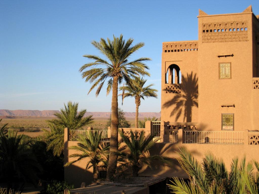 Ksar Oled Cherki的住宿－Auberge Ksar Jallal，沙漠中的一座建筑,前面有棕榈树