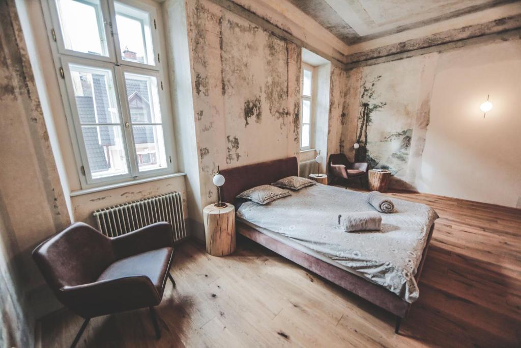 a bedroom with a bed and a chair and windows at Ruttner Suite in Veszprém