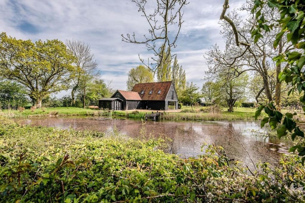 a house in a field next to a pond at Gardiners Cottage Barn in Eye