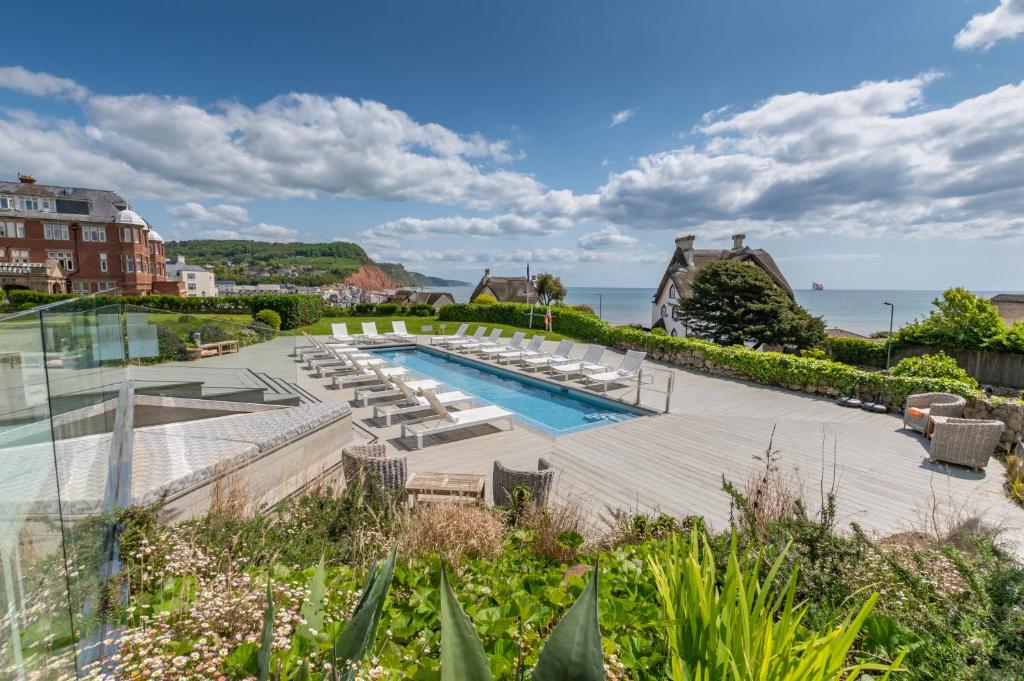 een zwembad met ligstoelen en de oceaan bij Harbour Hotel & Spa Sidmouth in Sidmouth