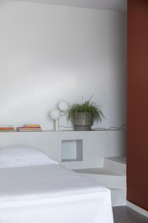 a white bedroom with a bed and a potted plant at Neo Suites in Fira