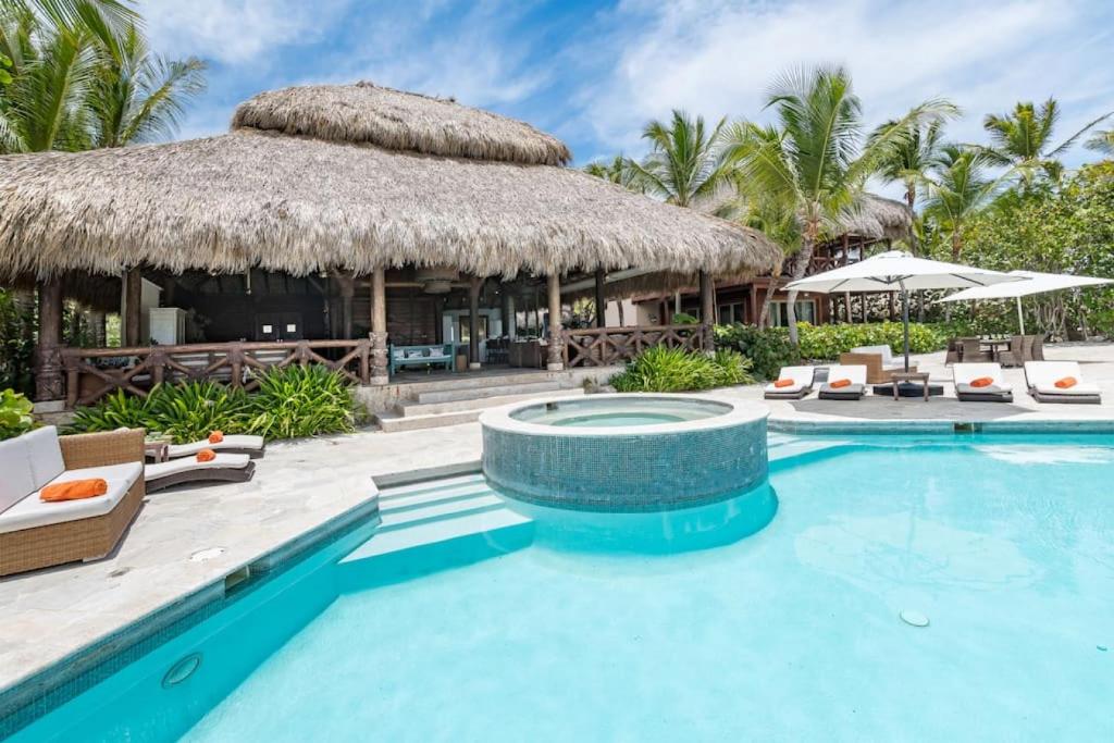 uma piscina de resort com cadeiras e um edifício com telhado de palha em CALETON 8 9 ACCESS TO EDEN ROC BEACH CLUB CHEF BUTLER MAiD GOLF CARTS POOLS JACUZZI em Punta Cana