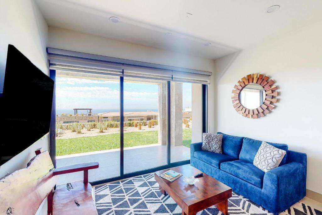 a living room with a blue couch and a large window at Tramonti Condo Tari #107 in Cabo San Lucas