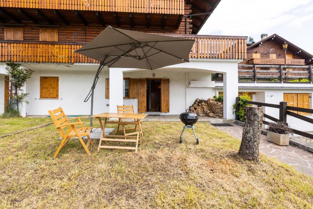 a patio with a table and chairs and an umbrella at Grazioso trilocale nel cuore di Folgaria in Folgaria