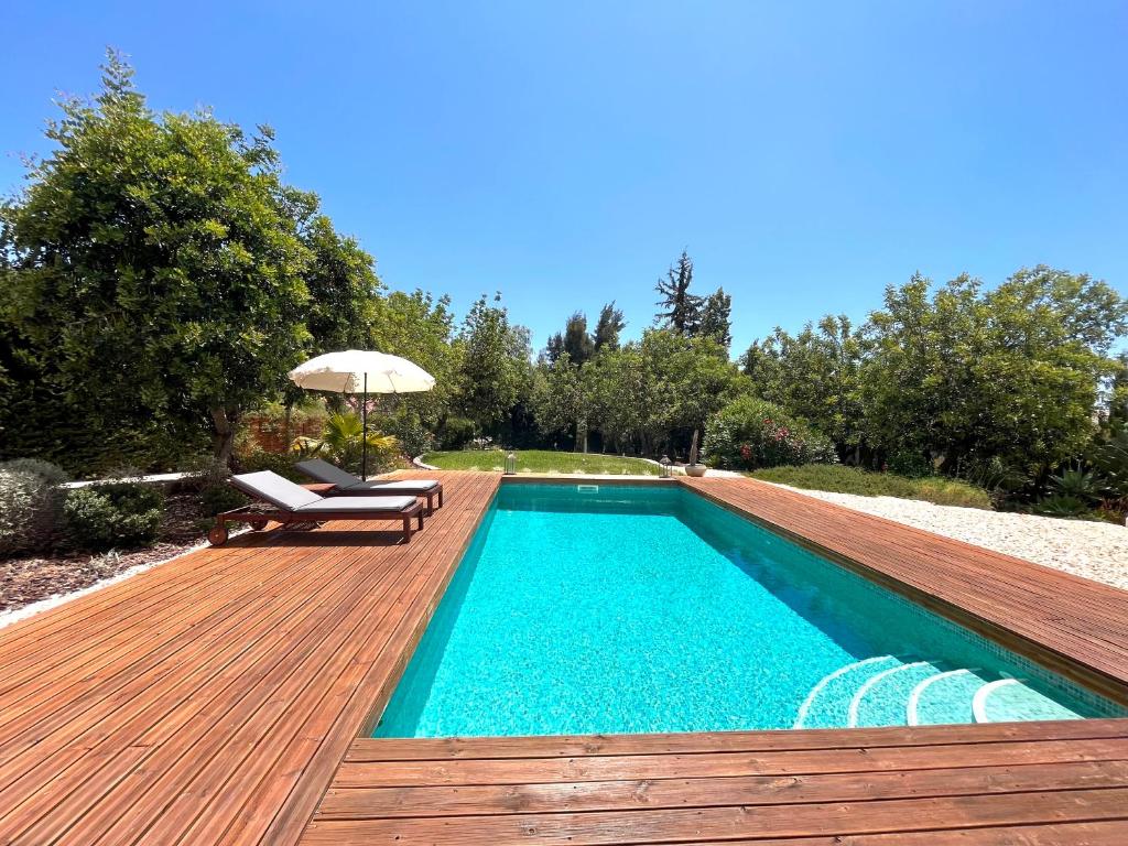 a swimming pool with a wooden deck and an umbrella at Quinta das Carpas in Tavira