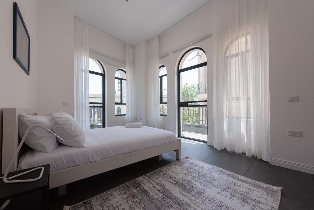 a white bedroom with windows and a bed and a rug at PORT CITY HAIFA - Flea Market Luxury in Haifa