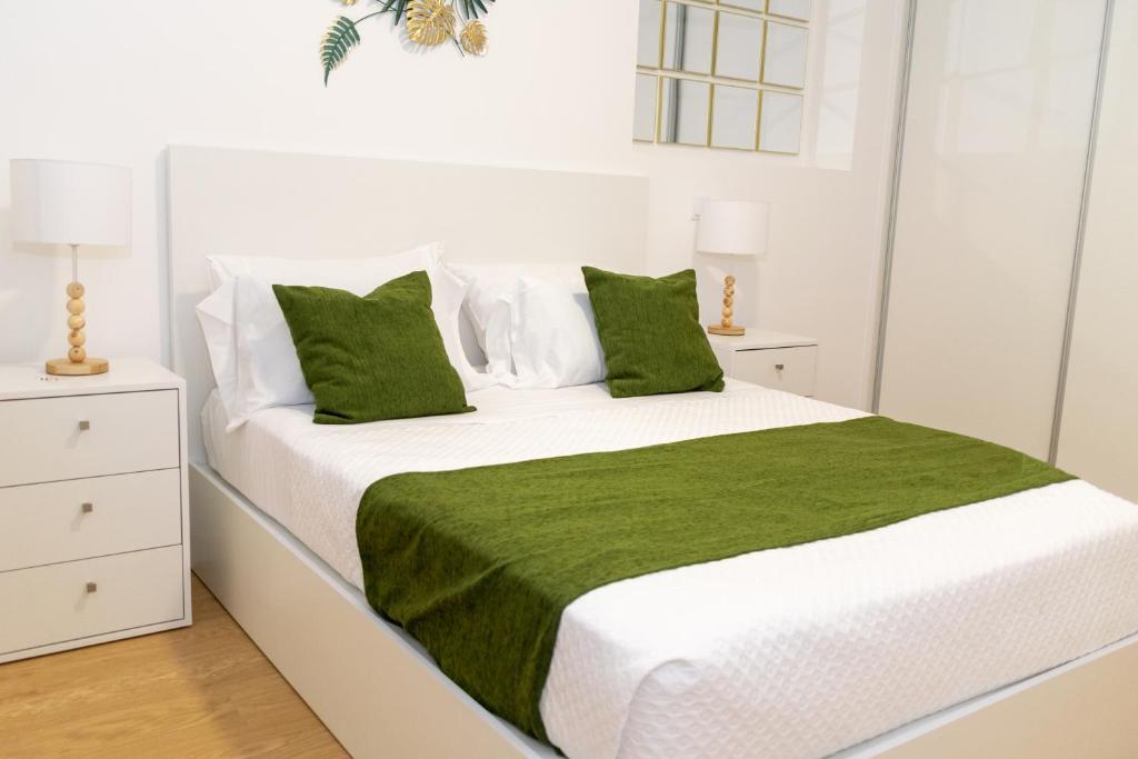 a white bedroom with a large white bed with green pillows at Sunscape Nature Apt de 1 quarto Ponta do Sol in Ponta do Sol