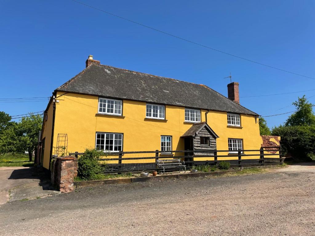 una casa amarilla con una valla delante de ella en Ashclyst Farm Rural Retreat en Exeter