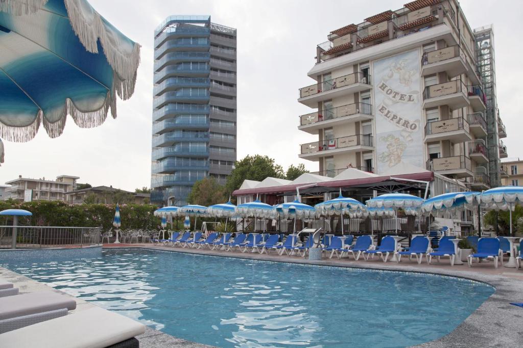 una piscina con sedie e ombrelloni e un edificio di Hotel Elpiro a Lido di Jesolo