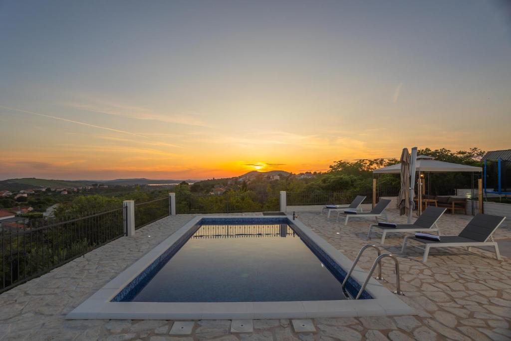 a pool with chairs and a sunset in the background at La casa Gidora in Šibenik