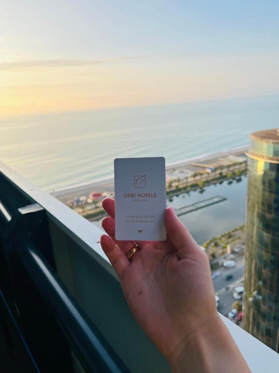 a person holding up a card in front of the ocean at #Orbi-city in Batumi