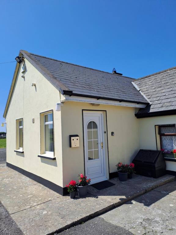 a small white building with a door and flowers at Doolin Farm Apartment in Doolin