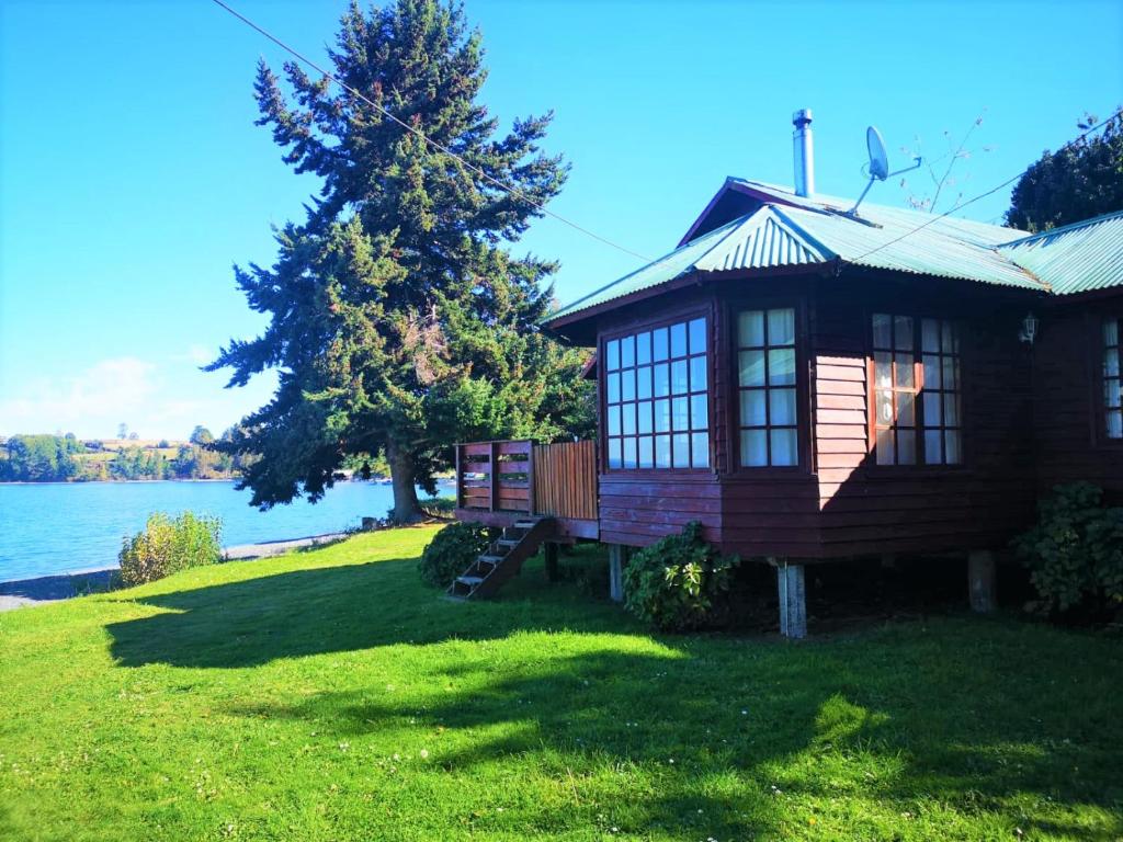 a log cabin on a lawn next to the water at Cabañas Los Bajos in Frutillar