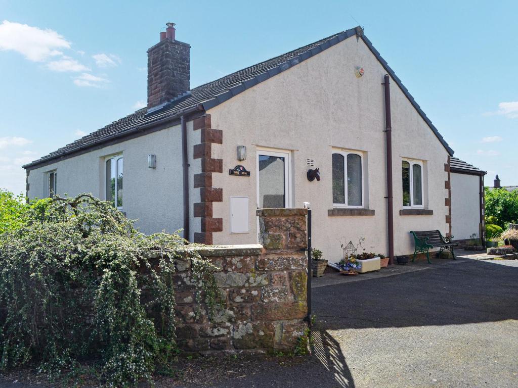 una pequeña casa blanca con una pared de ladrillo en Rose Rigg Cottage en Kirklinton