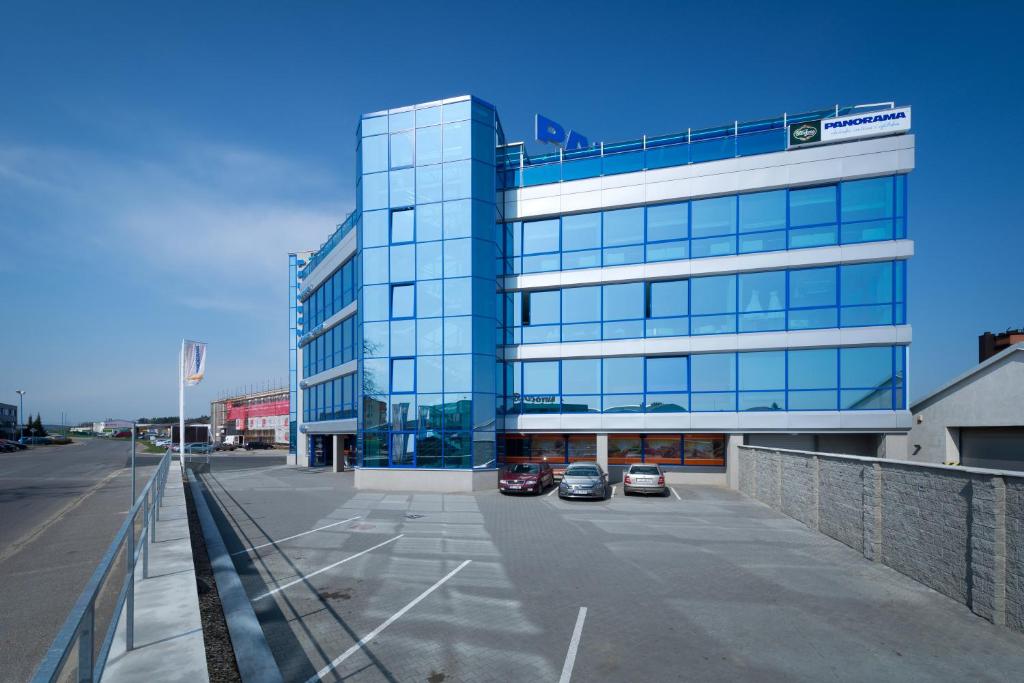een groot glazen gebouw met twee auto's geparkeerd op een parkeerplaats bij OC Panorama in Velké Meziříčí