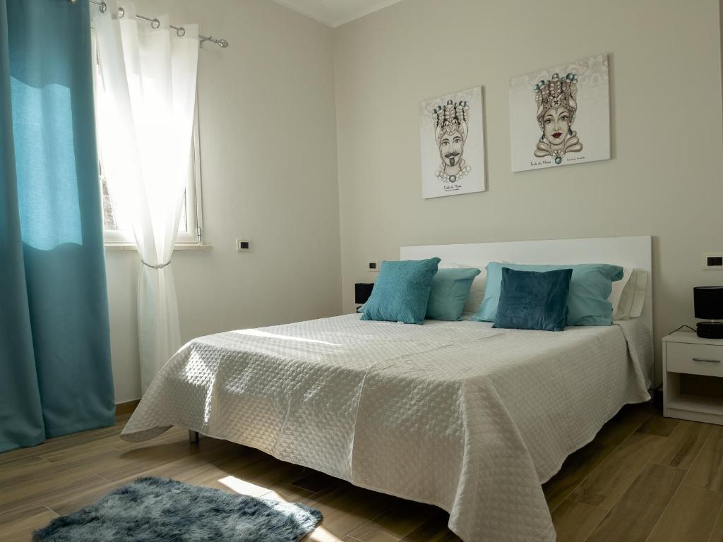 a white bedroom with a bed with blue pillows at Athena Agrigento Apartments in Agrigento
