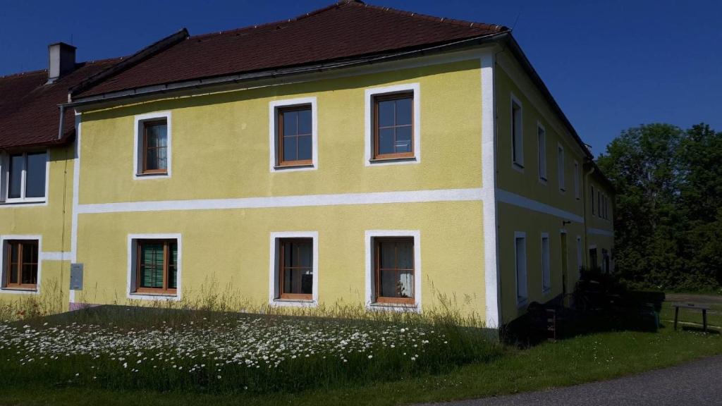 een geel huis met witte ramen en een bloemenveld bij Naturfreunde Alpenvorland in Kilb