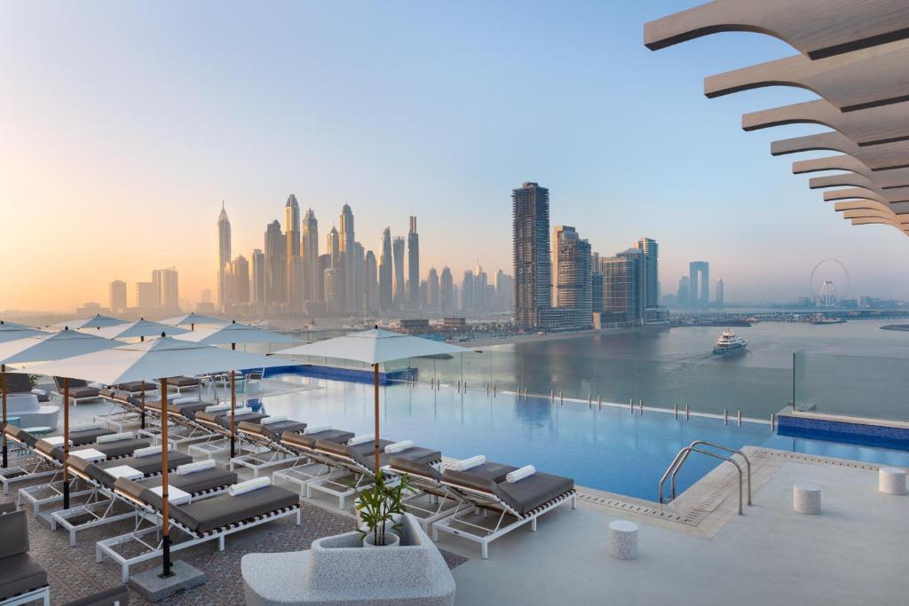 een zwembad met stoelen en parasols en een stad bij voco Dubai The Palm, an IHG Hotel in Dubai