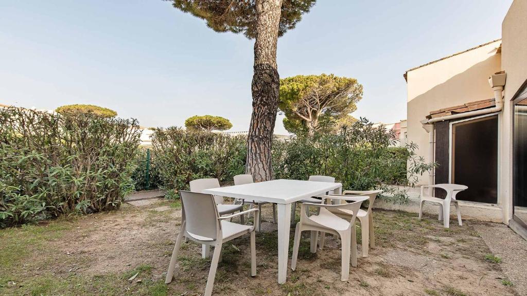 une table et des chaises blanches devant un arbre dans l'établissement Port Lano 112 - Appt cosy - 7 Personnes, au Cap d'Agde