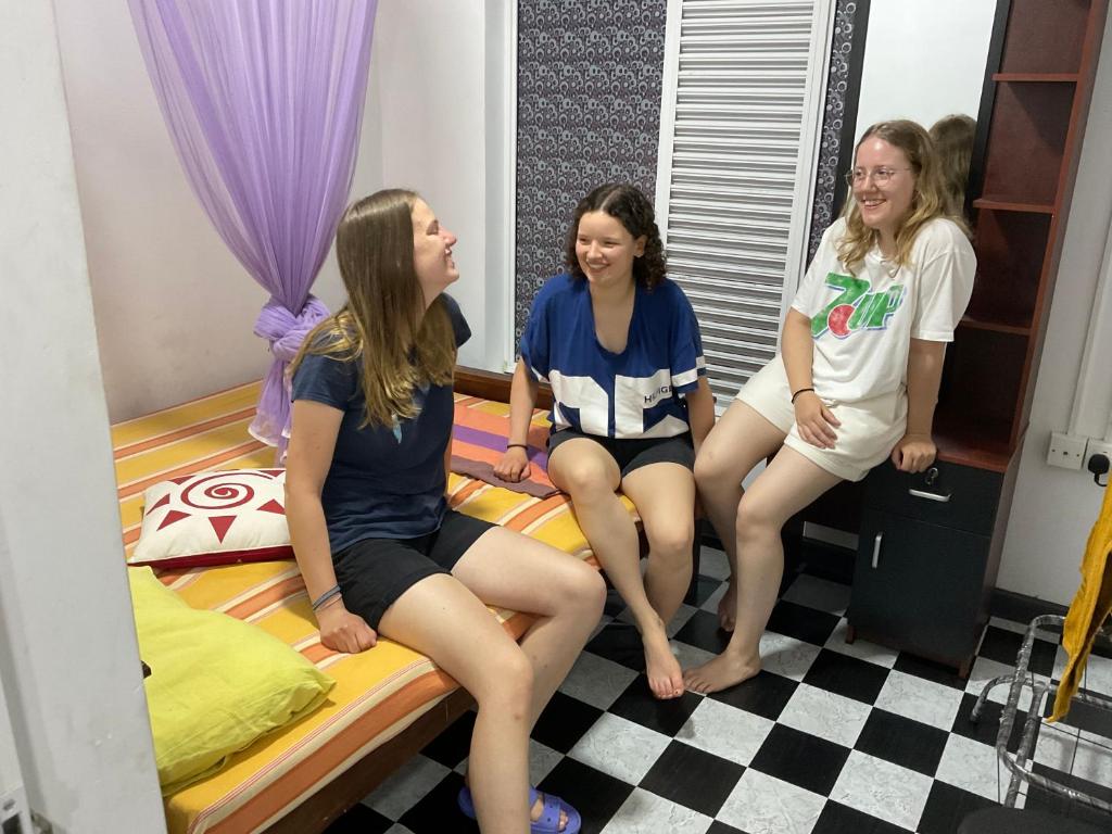 three girls sitting on a bed in a room at Robert Inn Dambulla in Dambulla