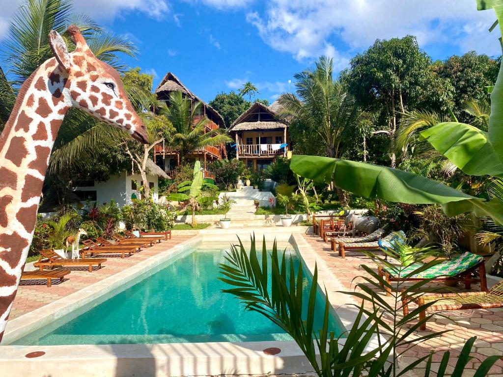 une girafe debout à côté d'une piscine dans l'établissement Kingstone lodge zanzibar, à Bet-el-Mali