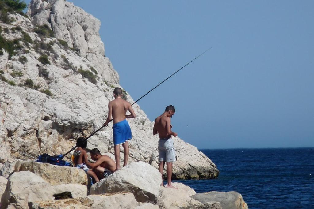 a group of men fishing on rocks near the ocean at Cabanon du Pêcheur, Parc National des Calanques in Marseille