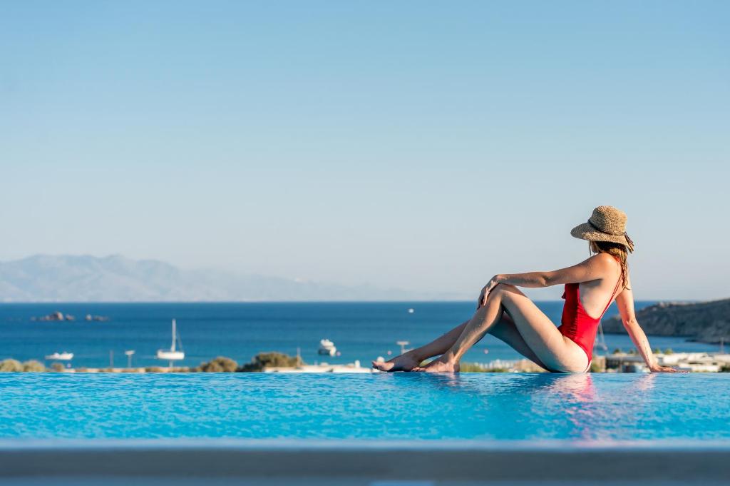 Una mujer con sombrero sentada en el agua en la playa en Mykonos4Islands Seaside Apartments, en Playa Kalo Livadi